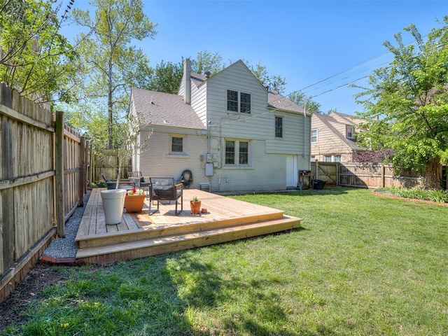rear view of house with a shingled roof, brick siding, a wooden deck, a fenced backyard, and a yard