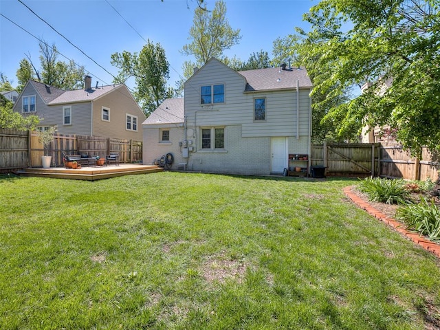 rear view of property with brick siding, a deck, a fenced backyard, and a lawn