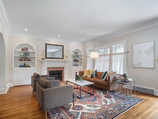 living room featuring built in features, a fireplace, wood finished floors, baseboards, and ornamental molding