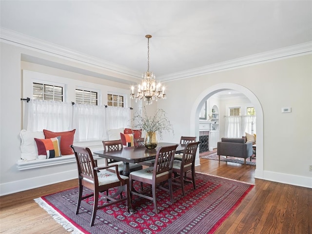 dining room with crown molding, arched walkways, wood finished floors, baseboards, and a chandelier