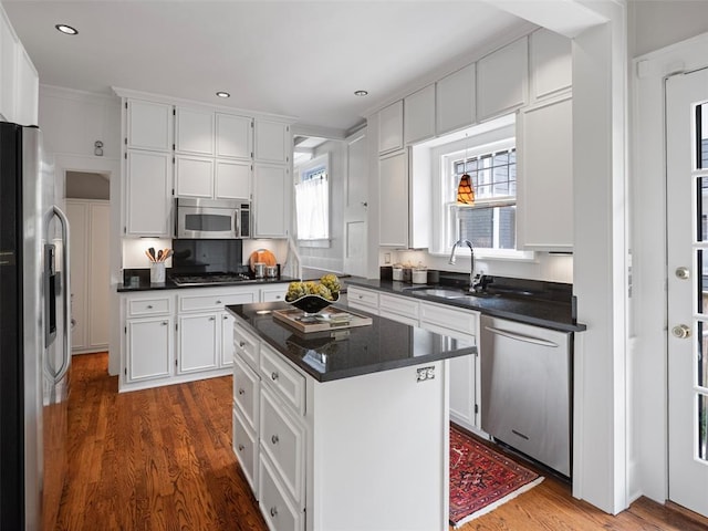 kitchen featuring white cabinets, dark countertops, a sink, stainless steel appliances, and wood finished floors