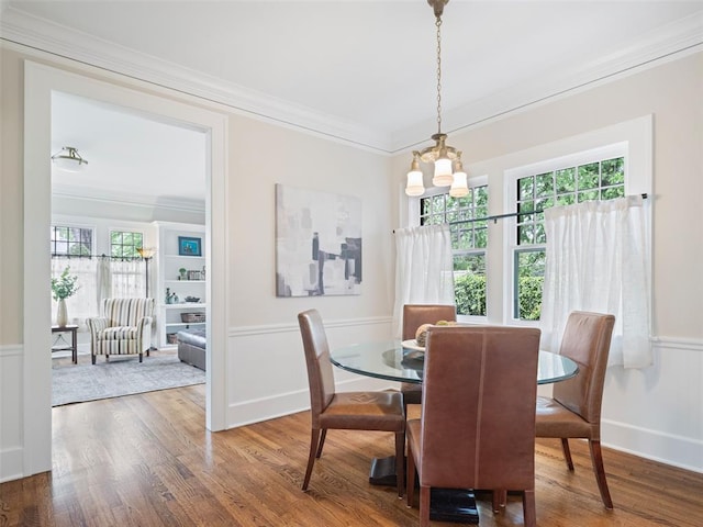 dining room with wood finished floors, a wainscoted wall, an inviting chandelier, ornamental molding, and a decorative wall