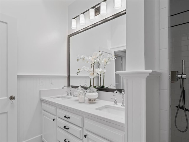full bathroom featuring a sink, a wainscoted wall, a tile shower, and double vanity