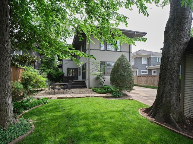 rear view of house featuring a patio, a yard, fence, and stucco siding