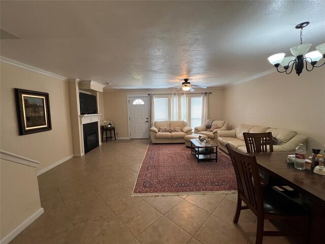 living area featuring crown molding, light tile patterned flooring, a fireplace, ceiling fan with notable chandelier, and baseboards