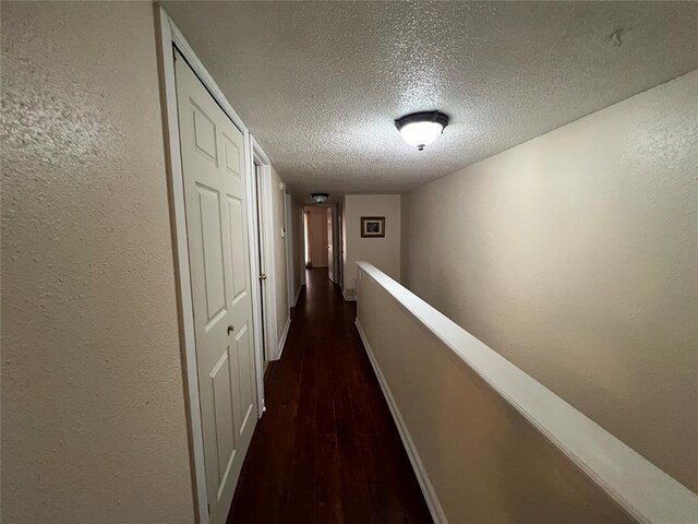 hall with a textured wall, baseboards, a textured ceiling, dark wood finished floors, and an upstairs landing