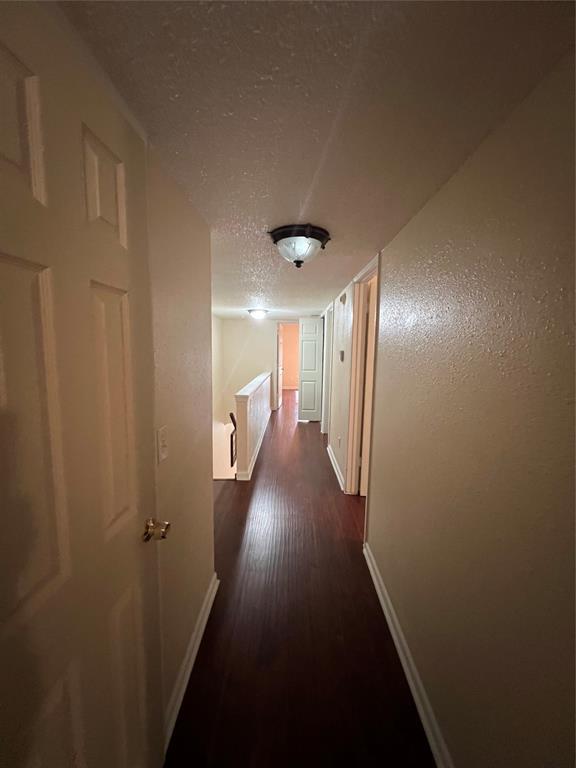 hallway featuring baseboards, dark wood-style floors, and a textured ceiling