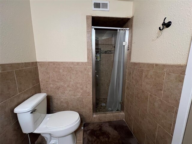 full bath featuring visible vents, tile walls, wainscoting, a stall shower, and toilet