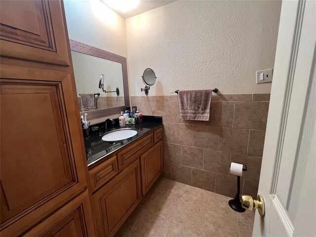 bathroom with vanity, a textured wall, a wainscoted wall, and tile walls