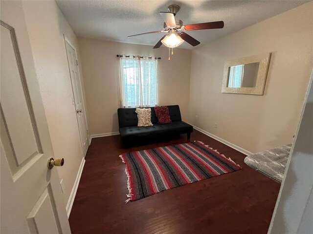 living area featuring baseboards, a ceiling fan, a textured ceiling, and wood finished floors