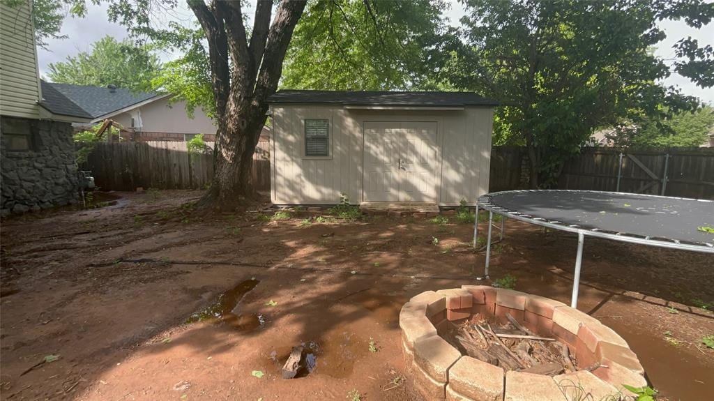 view of yard featuring a trampoline, a storage shed, an outdoor structure, a fenced backyard, and an outdoor fire pit