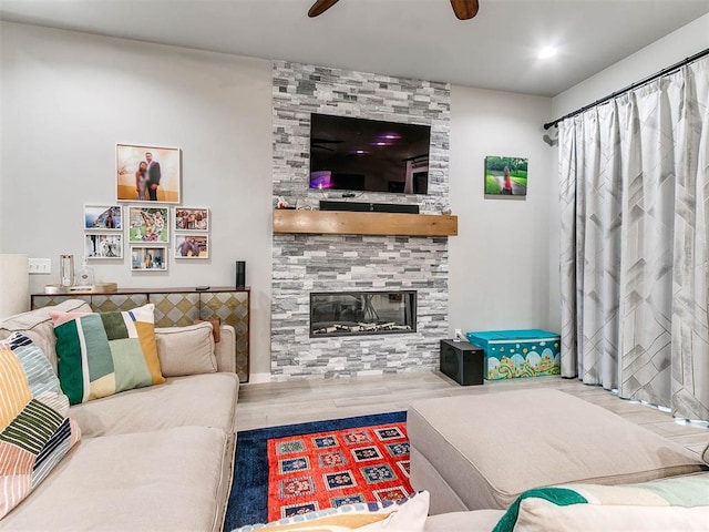 living room with a tiled fireplace, a ceiling fan, and wood finished floors