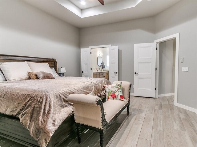 bedroom featuring a towering ceiling, baseboards, light wood-style floors, ensuite bathroom, and a tray ceiling