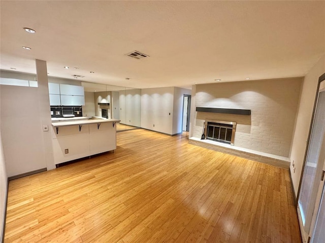 unfurnished living room featuring light wood finished floors, visible vents, baseboards, and a glass covered fireplace