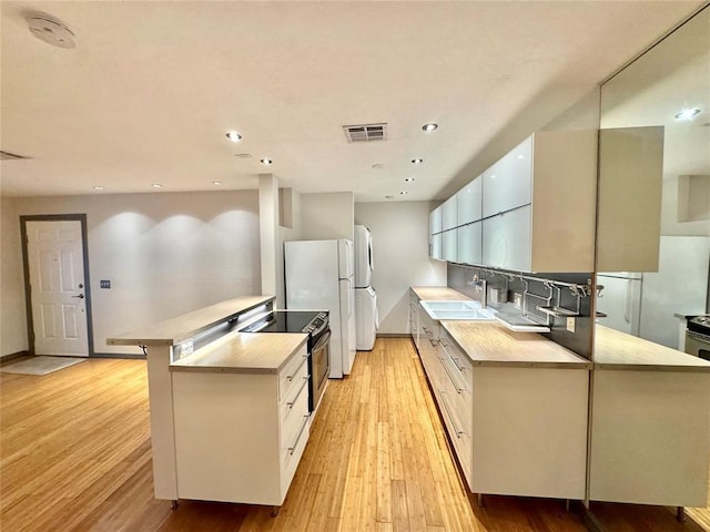 kitchen featuring light wood-style flooring, a peninsula, visible vents, and a sink