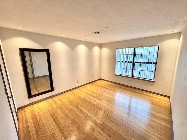 spare room with a textured ceiling, visible vents, wood finished floors, and baseboards