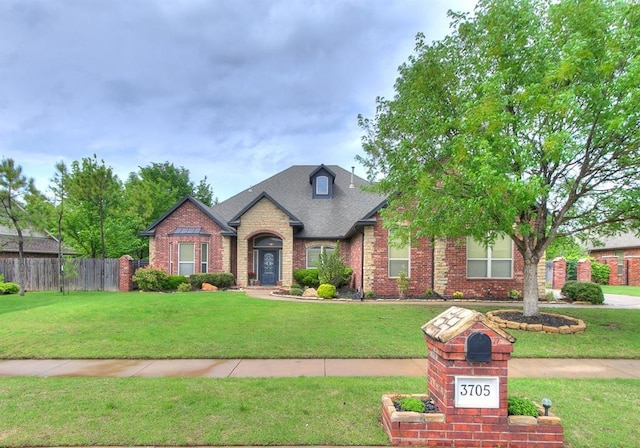 view of front of property featuring brick siding, fence, roof with shingles, and a front lawn