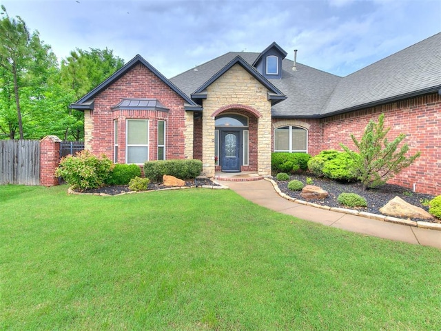 craftsman house with fence, a shingled roof, a front lawn, and stone siding