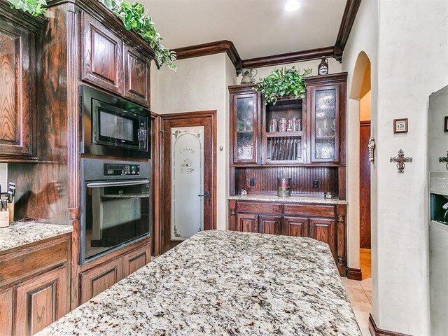 kitchen featuring crown molding, light stone counters, arched walkways, glass insert cabinets, and black appliances