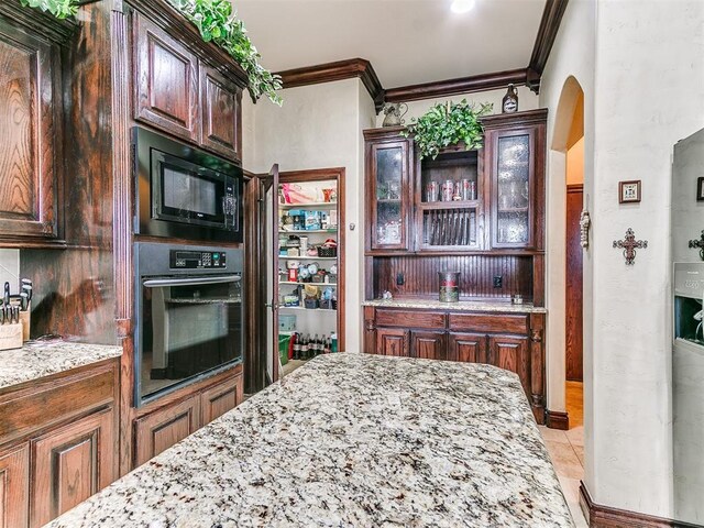 kitchen featuring arched walkways, ornamental molding, black appliances, and light stone counters