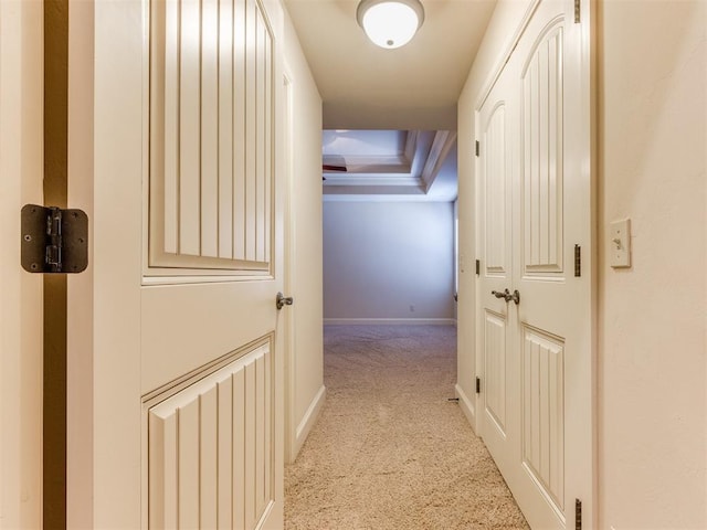 hallway featuring a raised ceiling, baseboards, and light carpet