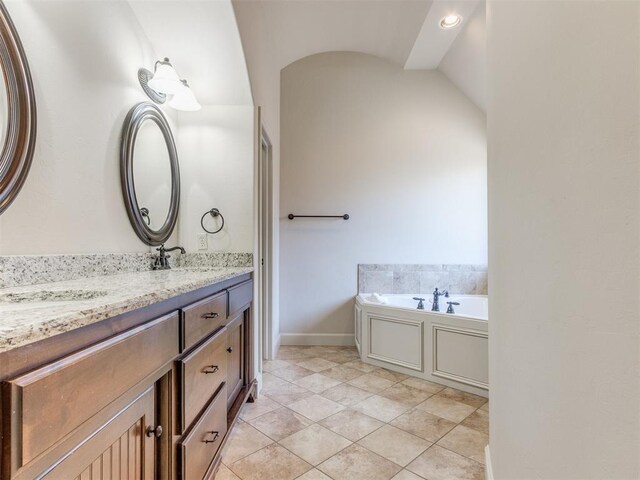 full bath with double vanity, baseboards, a bath, a sink, and vaulted ceiling