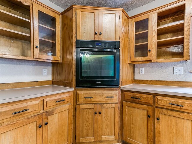 11817 Hollyrock Dr, Yukon, OK 73099 - kitchen featuring oven, a textured ceiling, glass insert cabinets, light countertops, and brown cabinets