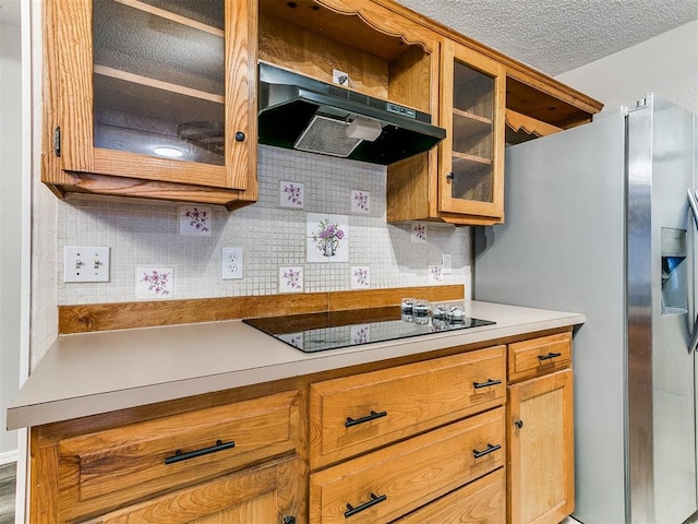 11817 Hollyrock Dr, Yukon, OK 73099 - kitchen featuring under cabinet range hood, black electric cooktop, tasteful backsplash, light countertops, and glass insert cabinets