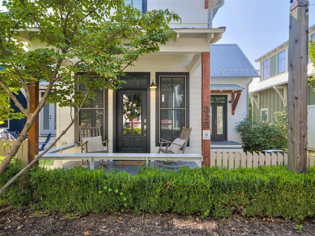 entrance to property featuring fence, covered porch, and metal roof