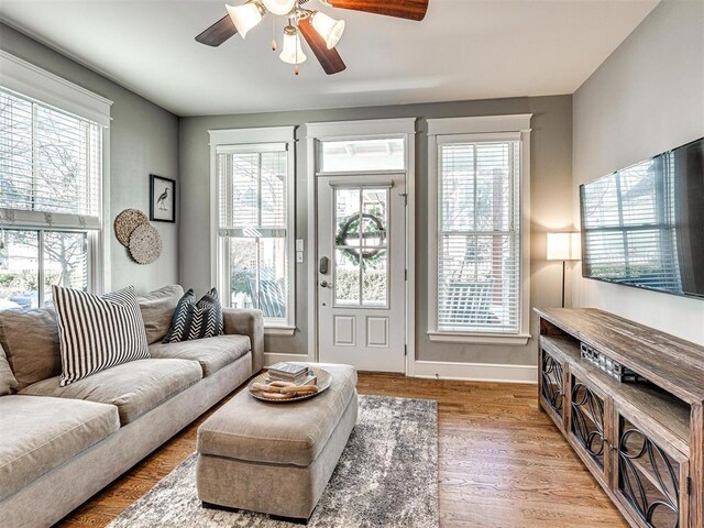 living area featuring baseboards, ceiling fan, and light wood-style flooring