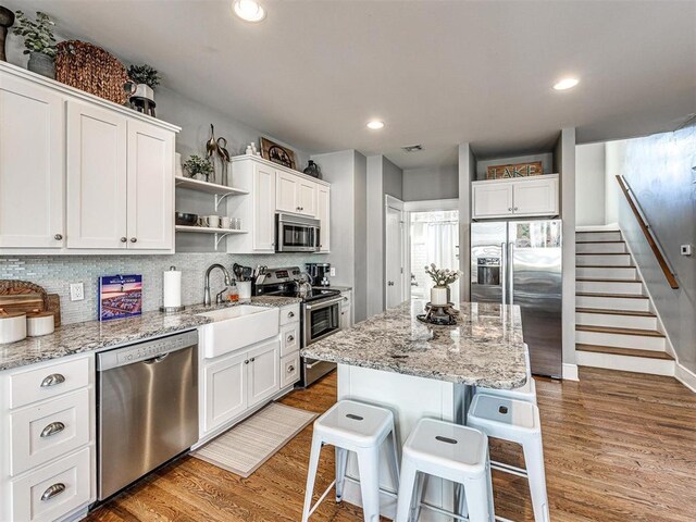 kitchen with open shelves, white cabinetry, a breakfast bar area, and stainless steel appliances