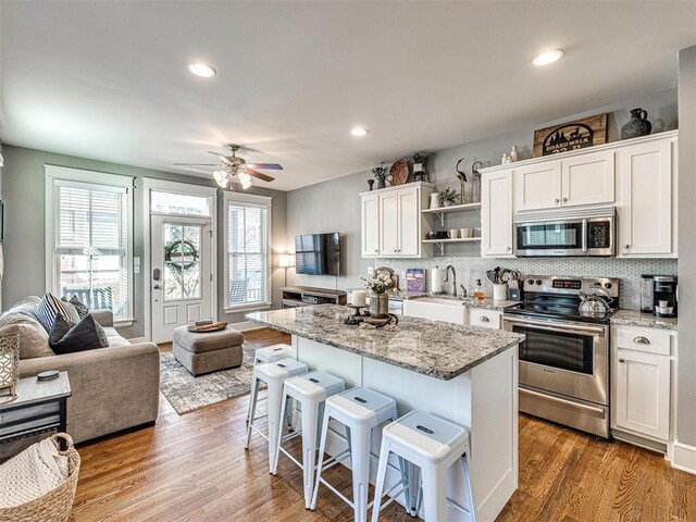 kitchen with a kitchen island, open shelves, wood finished floors, stainless steel appliances, and white cabinetry