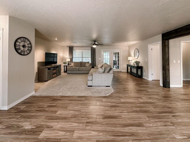 living room featuring baseboards, ceiling fan, a textured ceiling, and wood finished floors