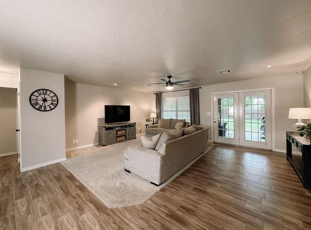 living room featuring a ceiling fan, a textured ceiling, visible vents, wood finished floors, and baseboards