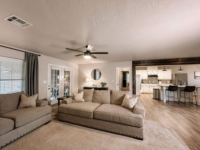 living room with a textured ceiling, visible vents, ceiling fan, and light wood-style flooring