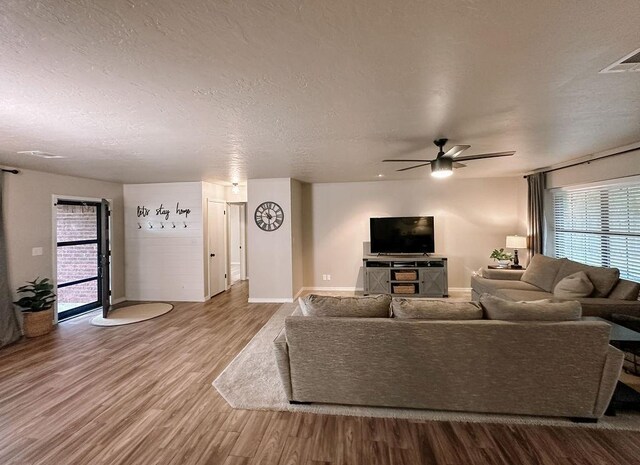 living room featuring ceiling fan, a textured ceiling, visible vents, wood finished floors, and baseboards