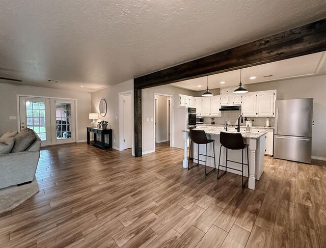 living area with a textured ceiling, wood finished floors, baseboards, beamed ceiling, and recessed lighting