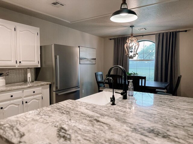 kitchen featuring visible vents, hanging light fixtures, freestanding refrigerator, a notable chandelier, and white cabinetry