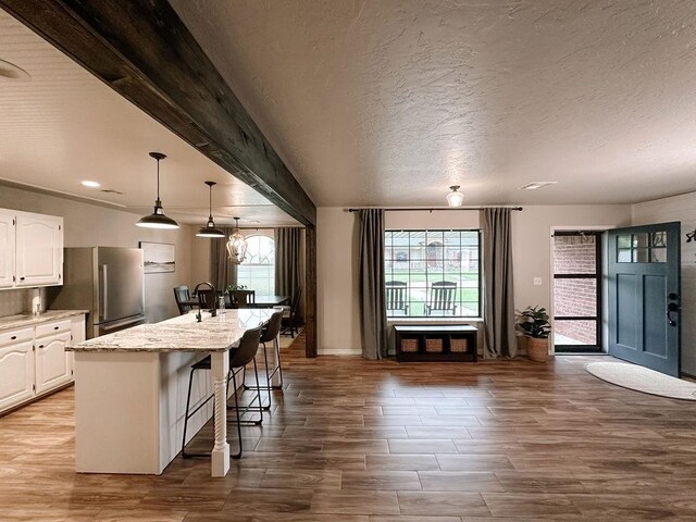 kitchen featuring freestanding refrigerator, wood finished floors, an island with sink, a kitchen bar, and white cabinets