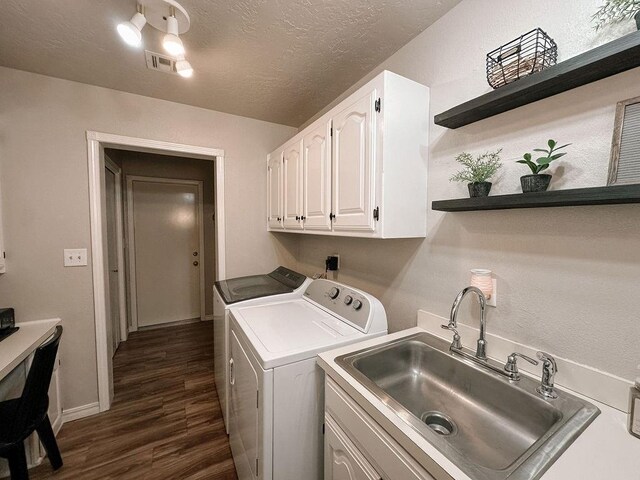 clothes washing area featuring a textured ceiling, washing machine and clothes dryer, cabinet space, a sink, and dark wood-type flooring