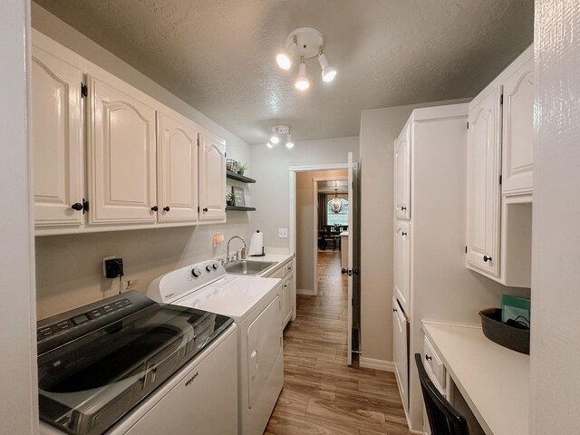 laundry room featuring a textured ceiling, washing machine and clothes dryer, cabinet space, a sink, and light wood finished floors