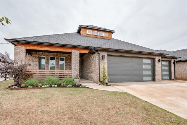 prairie-style home with brick siding, an attached garage, covered porch, and driveway