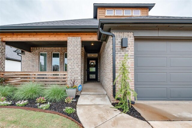 entrance to property featuring a shingled roof, an attached garage, and brick siding
