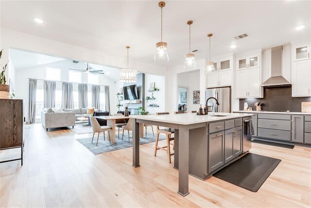 kitchen with wall chimney range hood, a sink, light countertops, gray cabinets, and visible vents
