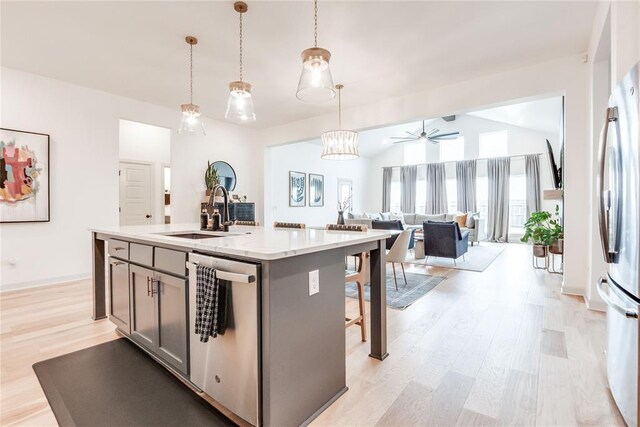 kitchen featuring a sink, light wood finished floors, stainless steel appliances, open floor plan, and pendant lighting