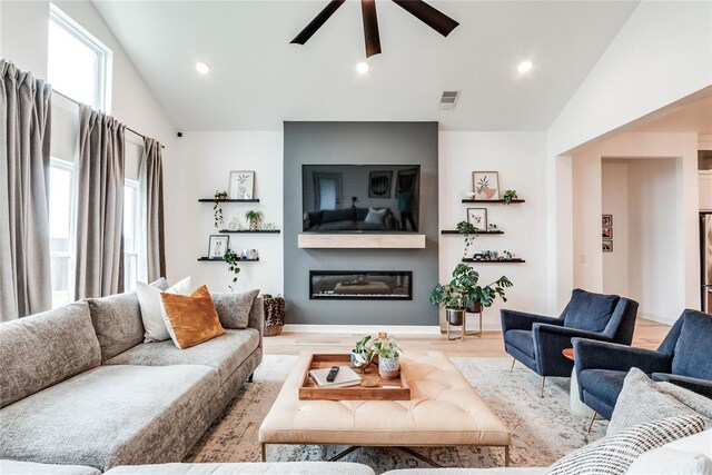 living room featuring visible vents, a glass covered fireplace, wood finished floors, lofted ceiling, and ceiling fan