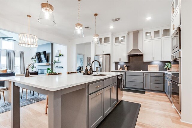 kitchen with wall chimney range hood, appliances with stainless steel finishes, gray cabinetry, light wood finished floors, and white cabinetry
