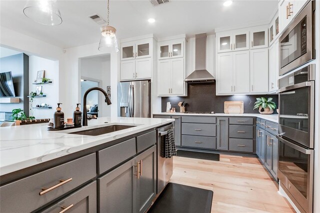 kitchen with wall chimney range hood, visible vents, gray cabinetry, a sink, and stainless steel appliances