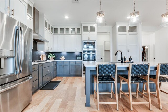 kitchen featuring wall chimney range hood, light countertops, a sink, light wood-style flooring, and appliances with stainless steel finishes