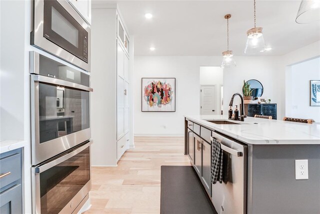 kitchen with decorative light fixtures, stainless steel appliances, light stone countertops, and a sink